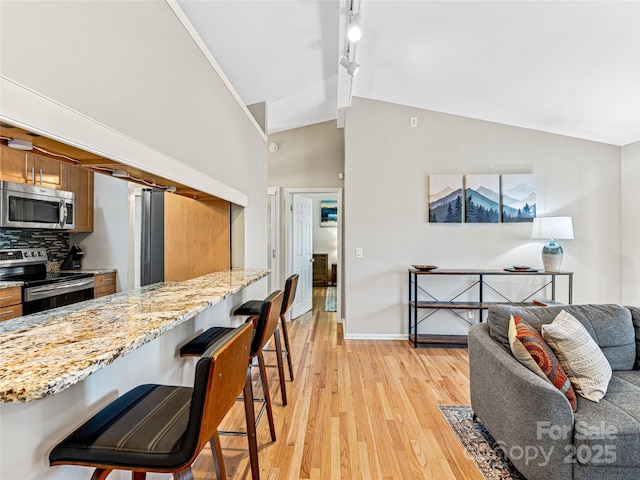 kitchen featuring stainless steel appliances, a kitchen breakfast bar, light stone counters, vaulted ceiling, and light wood-type flooring