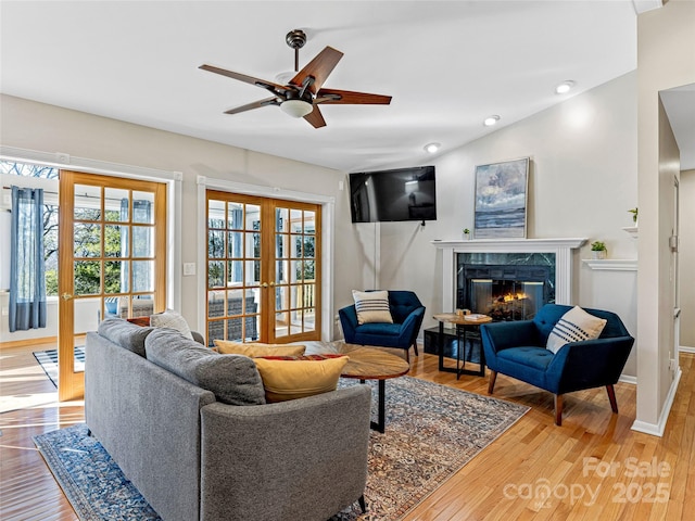 living room featuring hardwood / wood-style flooring, a premium fireplace, ceiling fan, and french doors