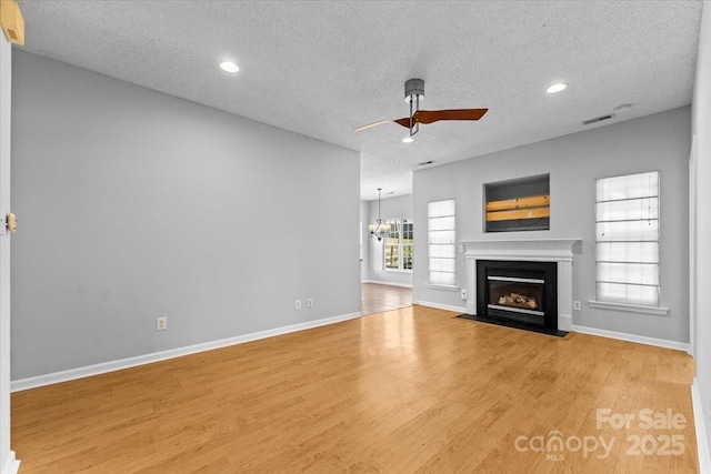 unfurnished living room featuring hardwood / wood-style floors, ceiling fan with notable chandelier, and a textured ceiling