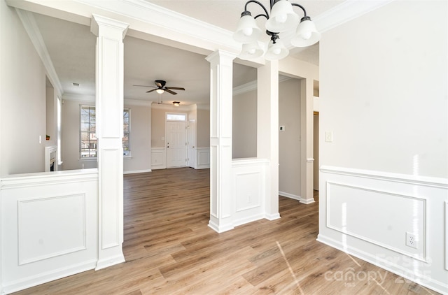 spare room featuring ceiling fan with notable chandelier, light wood-style floors, wainscoting, decorative columns, and crown molding