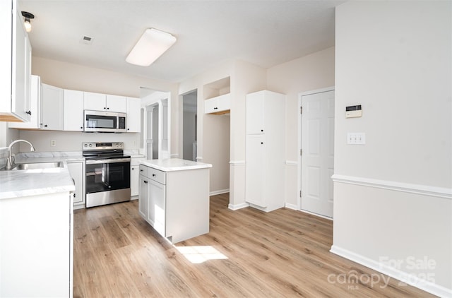 kitchen with appliances with stainless steel finishes, a center island, light countertops, white cabinetry, and a sink