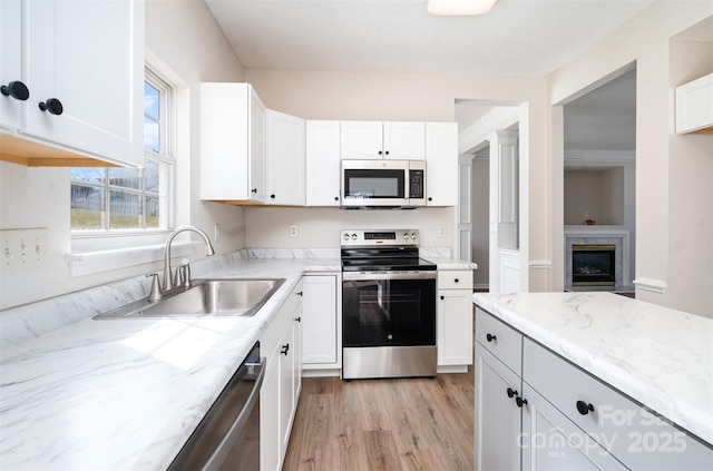 kitchen featuring light stone counters, white cabinetry, stainless steel appliances, and a sink