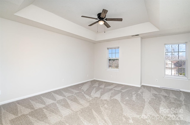 unfurnished room with carpet flooring, a raised ceiling, visible vents, and baseboards