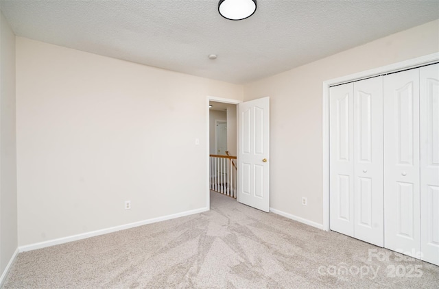 unfurnished bedroom with light carpet, a closet, a textured ceiling, and baseboards