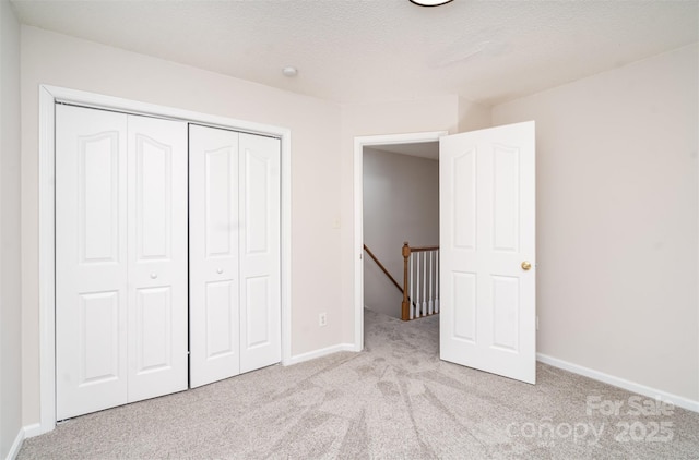 unfurnished bedroom featuring light carpet, a closet, a textured ceiling, and baseboards