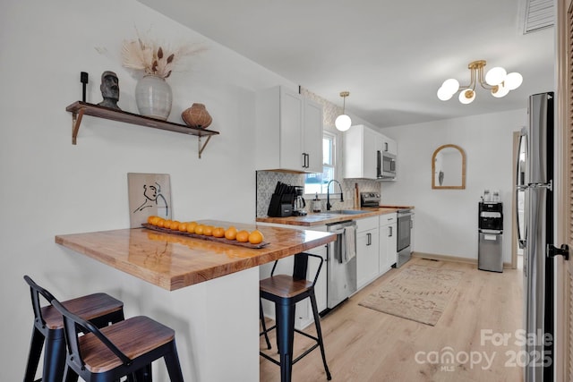 kitchen featuring appliances with stainless steel finishes, butcher block counters, a breakfast bar area, and white cabinets