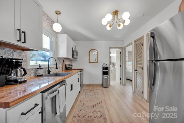 kitchen featuring white cabinetry, appliances with stainless steel finishes, butcher block countertops, and decorative light fixtures