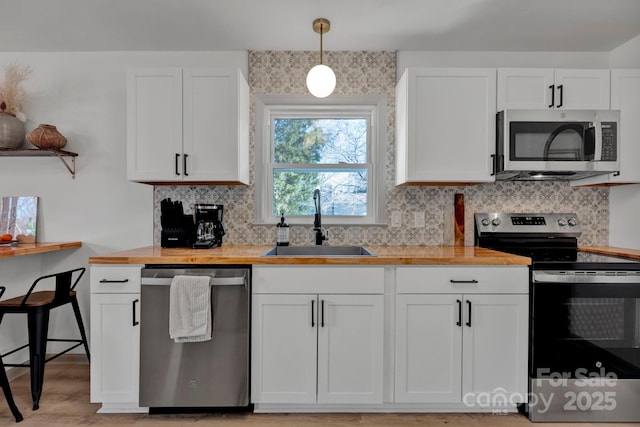 kitchen featuring appliances with stainless steel finishes, wood counters, white cabinetry, sink, and hanging light fixtures