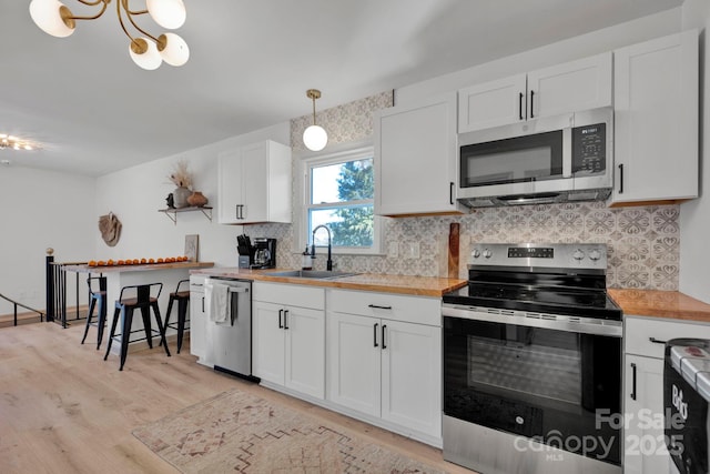 kitchen featuring pendant lighting, sink, white cabinetry, butcher block counters, and stainless steel appliances