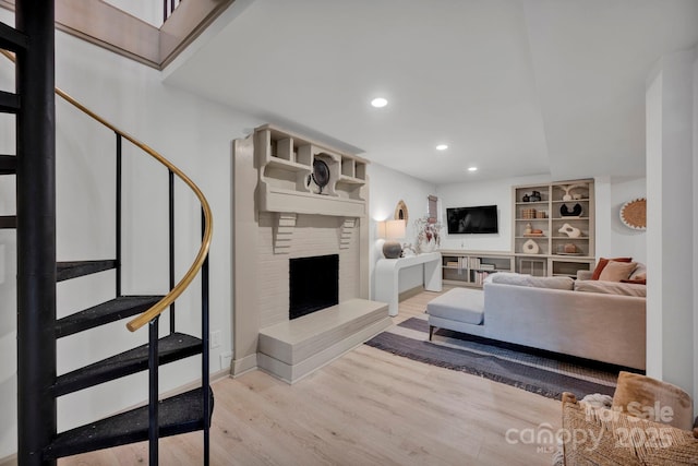 living room featuring built in shelves, a fireplace, and light hardwood / wood-style floors