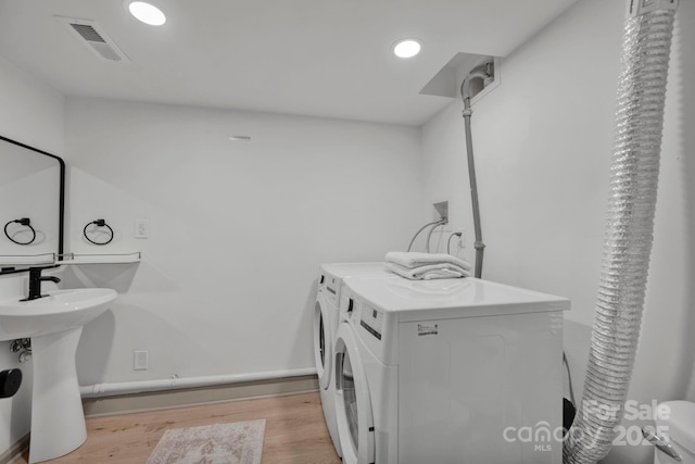 laundry room featuring sink, washing machine and dryer, and light hardwood / wood-style flooring