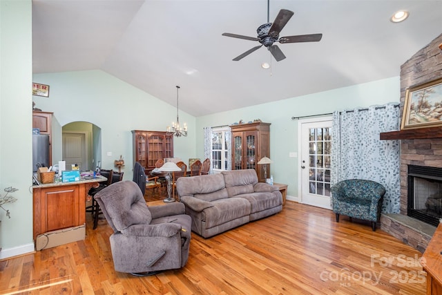 living room with ceiling fan with notable chandelier, vaulted ceiling, a stone fireplace, and light hardwood / wood-style flooring