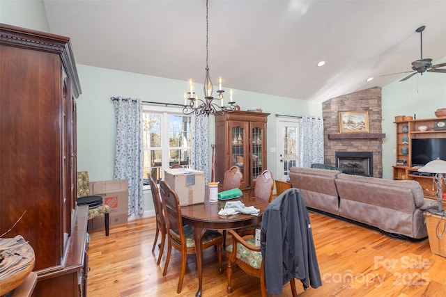 dining space with ceiling fan with notable chandelier, lofted ceiling, light hardwood / wood-style flooring, and a stone fireplace