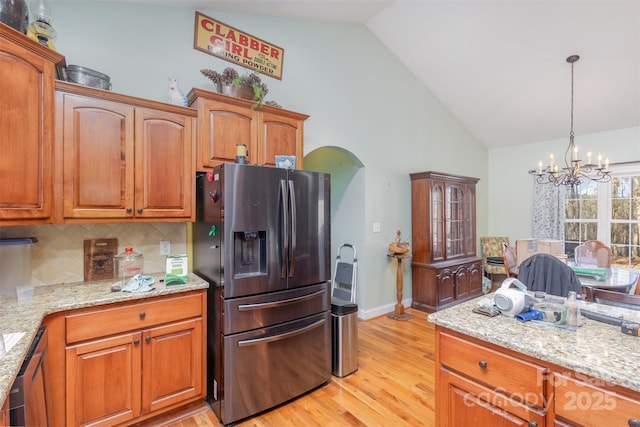 kitchen featuring light stone countertops, light hardwood / wood-style flooring, stainless steel refrigerator with ice dispenser, a notable chandelier, and decorative backsplash