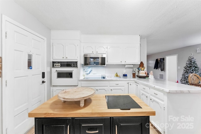 kitchen with white cabinets, oven, kitchen peninsula, and a textured ceiling