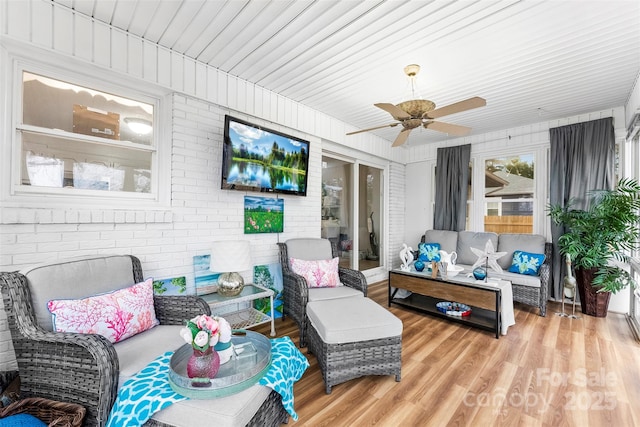 living room featuring ceiling fan, brick wall, and light wood-type flooring