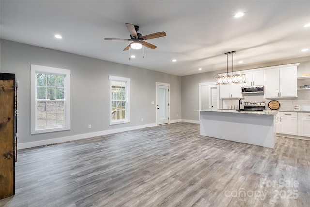 kitchen featuring appliances with stainless steel finishes, pendant lighting, a center island with sink, white cabinets, and light wood-type flooring