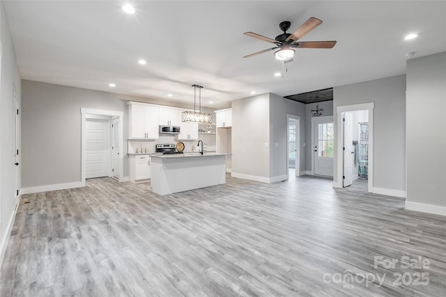 kitchen featuring hanging light fixtures, stainless steel appliances, a center island with sink, white cabinets, and light wood-type flooring