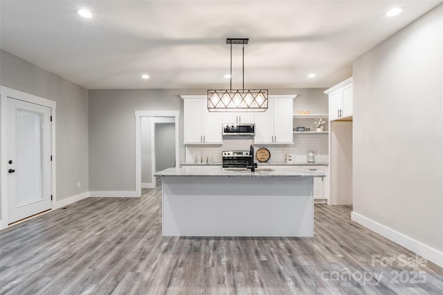 kitchen with hanging light fixtures, light stone countertops, an island with sink, white cabinetry, and stainless steel appliances