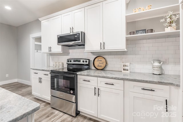 kitchen with backsplash, light stone counters, stainless steel appliances, white cabinets, and light hardwood / wood-style floors