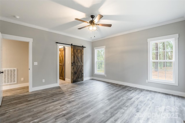 unfurnished bedroom featuring a barn door, ceiling fan, crown molding, and hardwood / wood-style floors