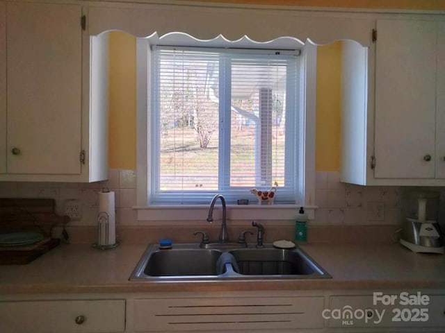 kitchen featuring light countertops, backsplash, a sink, and white cabinetry