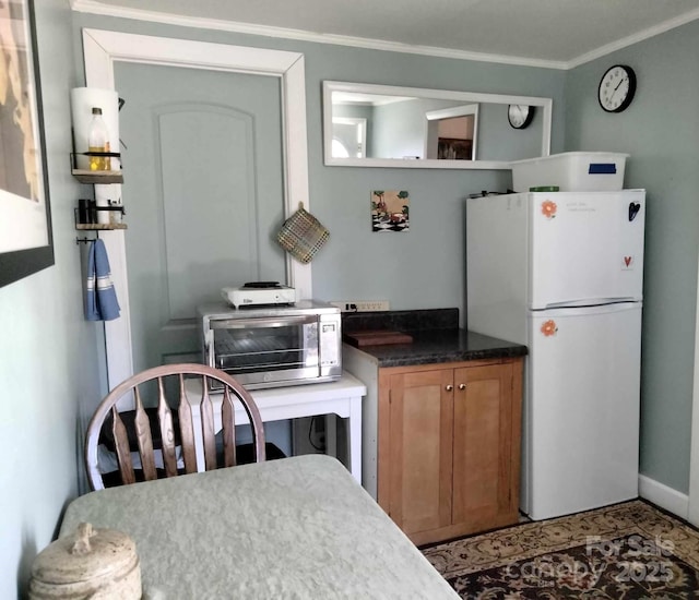 kitchen featuring a toaster, dark countertops, ornamental molding, brown cabinets, and freestanding refrigerator