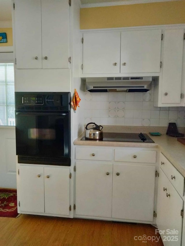 kitchen with tasteful backsplash, under cabinet range hood, light wood-type flooring, black appliances, and white cabinetry