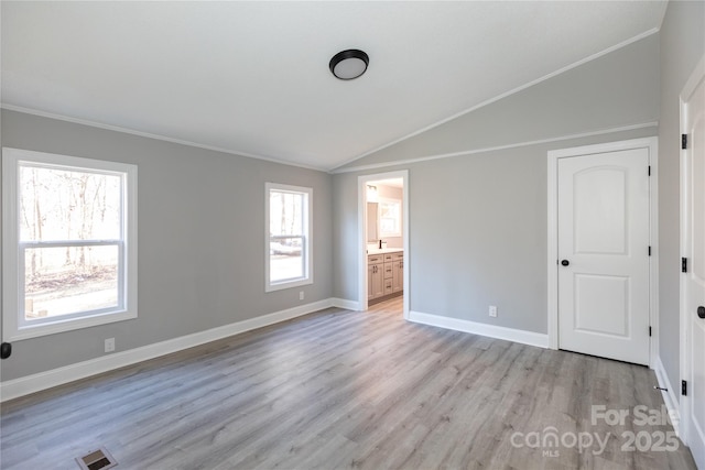 unfurnished bedroom featuring ensuite bath, light hardwood / wood-style flooring, vaulted ceiling, and ornamental molding