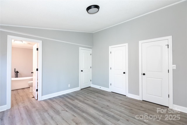 unfurnished bedroom featuring ensuite bathroom, light hardwood / wood-style floors, vaulted ceiling, and ornamental molding