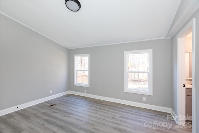 spare room featuring light hardwood / wood-style floors, crown molding, and vaulted ceiling