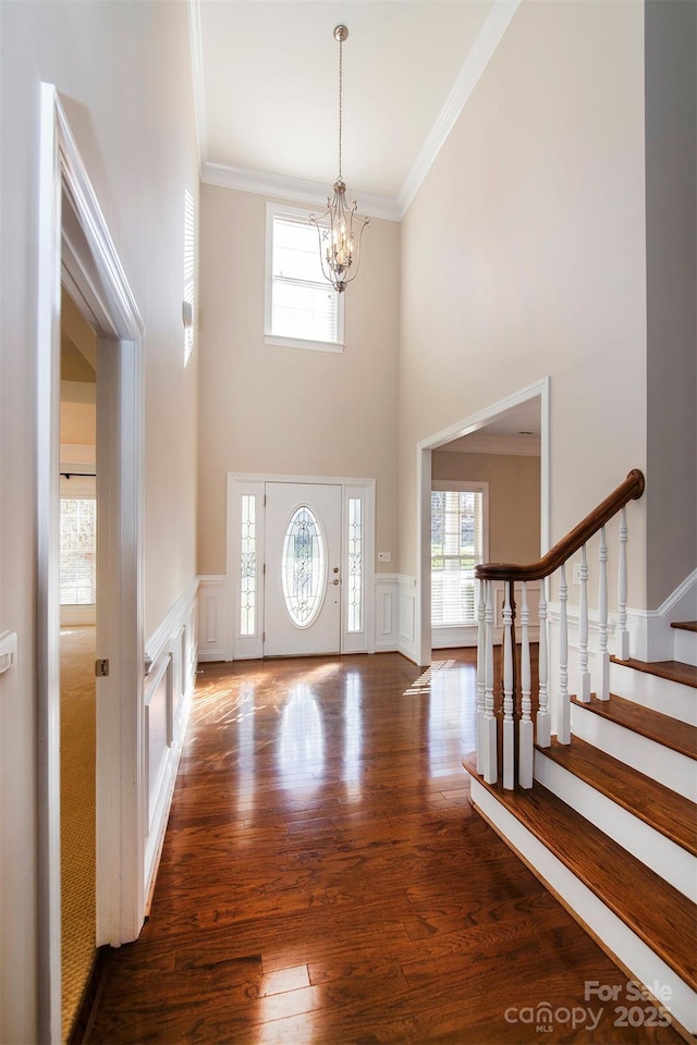 foyer entrance with a notable chandelier, ornamental molding, a towering ceiling, and dark hardwood / wood-style floors