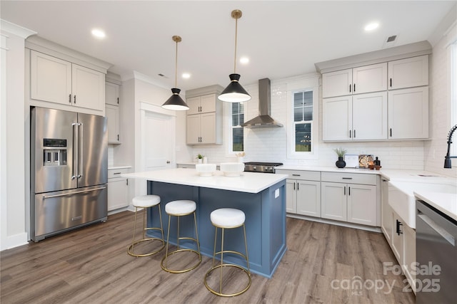 kitchen featuring hardwood / wood-style floors, a center island, hanging light fixtures, wall chimney exhaust hood, and appliances with stainless steel finishes