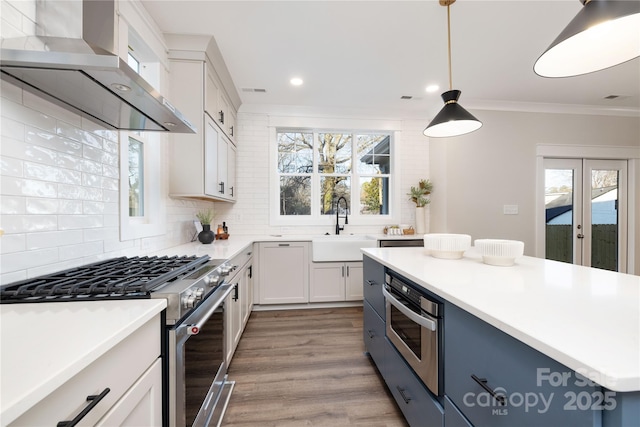 kitchen featuring pendant lighting, white cabinets, sink, wall chimney exhaust hood, and stainless steel appliances