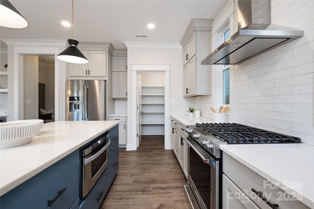 kitchen featuring hanging light fixtures, wall chimney exhaust hood, decorative backsplash, ornamental molding, and stainless steel appliances