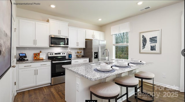 kitchen featuring white cabinetry, sink, stainless steel appliances, backsplash, and a kitchen island with sink