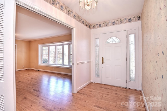 foyer with light hardwood / wood-style floors, crown molding, and a chandelier