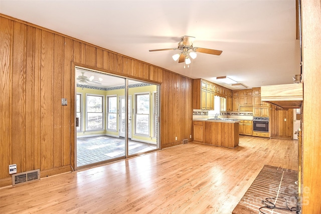 kitchen with ceiling fan, sink, light hardwood / wood-style flooring, wood walls, and oven