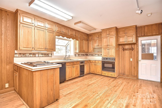 kitchen with kitchen peninsula, sink, black appliances, light hardwood / wood-style flooring, and wood walls