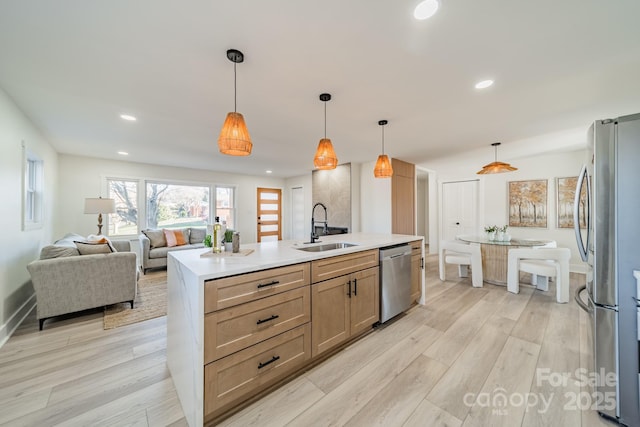 kitchen with appliances with stainless steel finishes, sink, light hardwood / wood-style floors, hanging light fixtures, and an island with sink