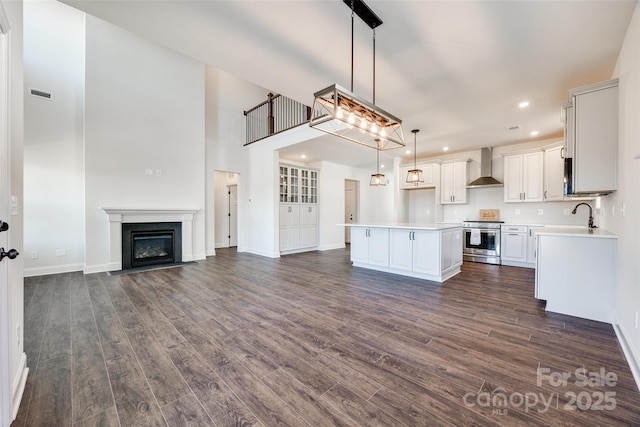 kitchen with dark wood finished floors, light countertops, electric range, a kitchen island, and wall chimney exhaust hood