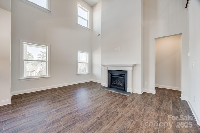 unfurnished living room with dark wood-type flooring, plenty of natural light, a fireplace with flush hearth, and baseboards