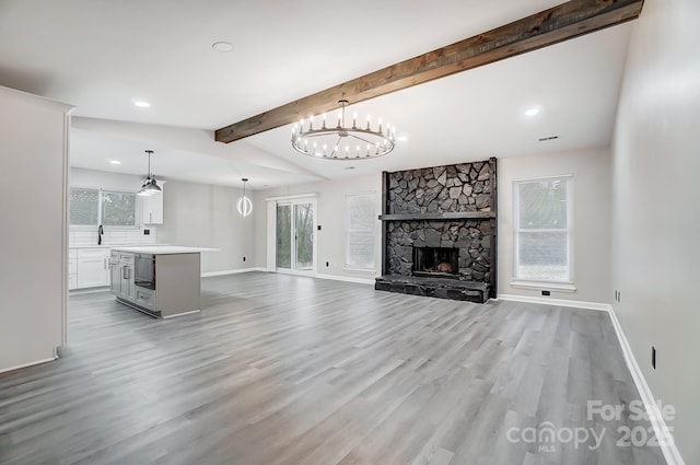 unfurnished living room featuring a fireplace, light wood-type flooring, vaulted ceiling with beams, and a notable chandelier