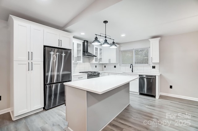 kitchen featuring stainless steel appliances, a center island, pendant lighting, wall chimney exhaust hood, and white cabinets