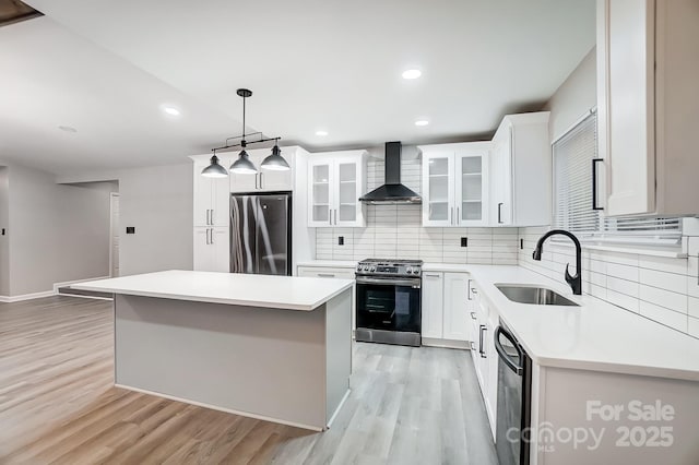 kitchen with stainless steel appliances, hanging light fixtures, a center island, white cabinets, and wall chimney range hood