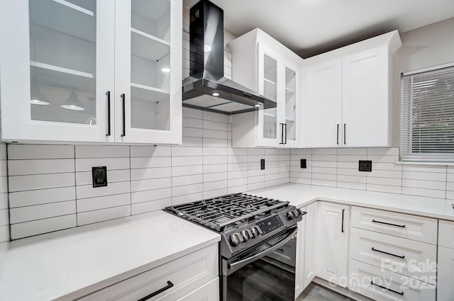 kitchen featuring white cabinetry, range with gas cooktop, decorative backsplash, and wall chimney exhaust hood