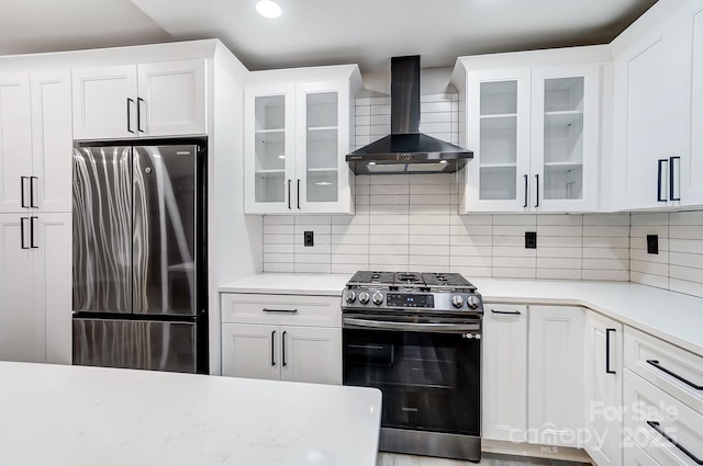 kitchen with appliances with stainless steel finishes, white cabinetry, wall chimney range hood, and backsplash