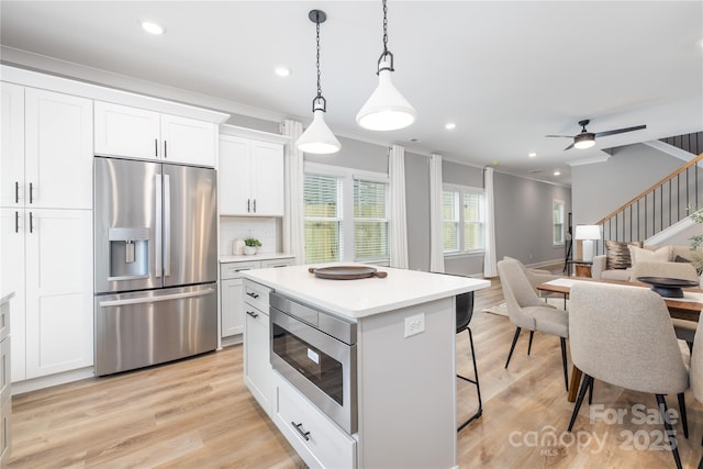 kitchen with decorative backsplash, appliances with stainless steel finishes, ornamental molding, white cabinetry, and hanging light fixtures