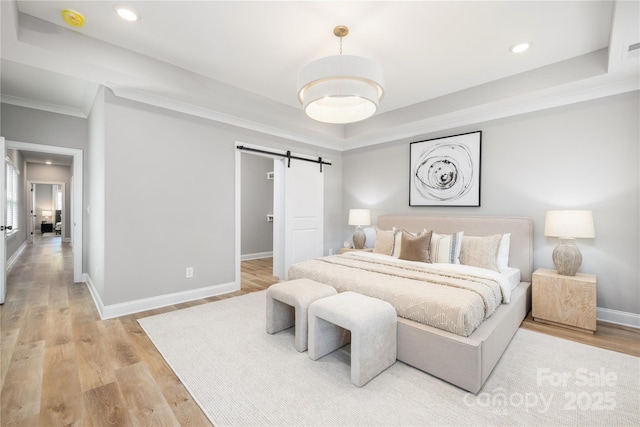 bedroom with hardwood / wood-style floors, a barn door, a raised ceiling, and crown molding