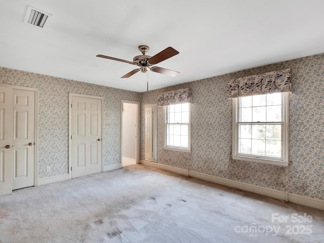 unfurnished bedroom featuring ceiling fan, light colored carpet, and two closets